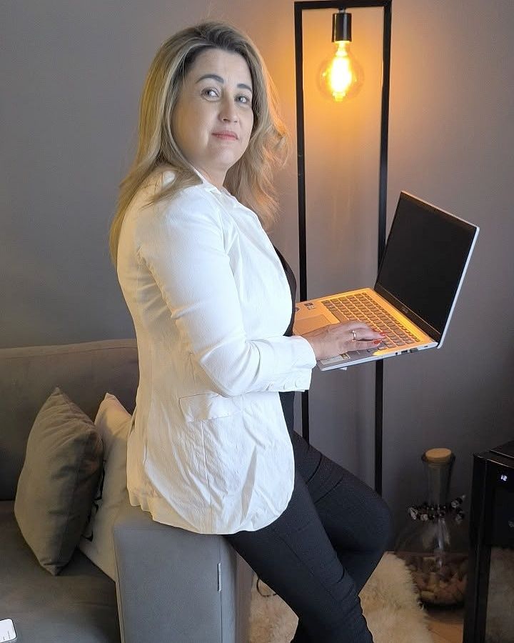 Adriana Silva sentada no braço de um sofá, com o notebook aberto na mão.